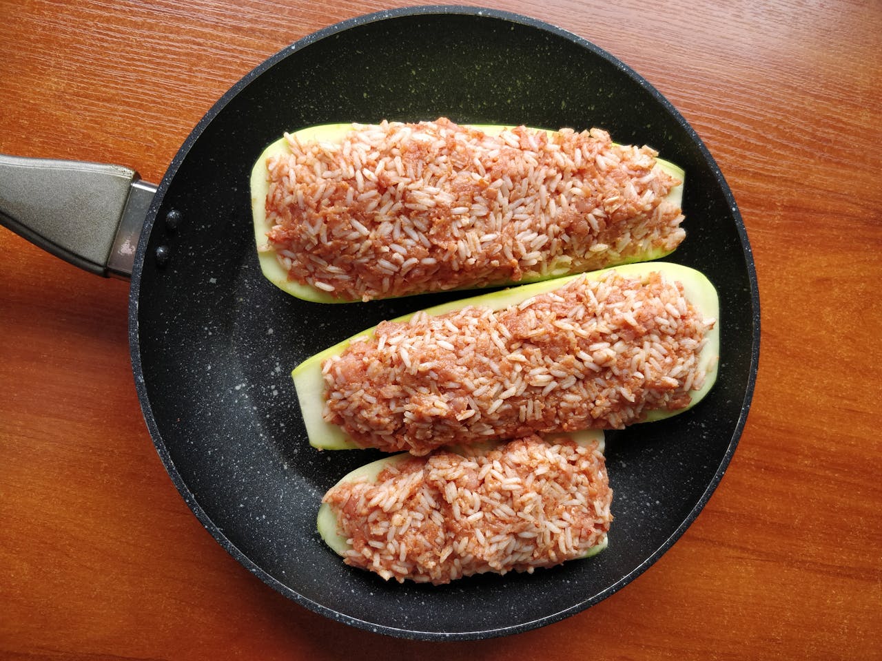 digital Appetizing stuffed zucchini with rice, served in a skillet on a wooden table.