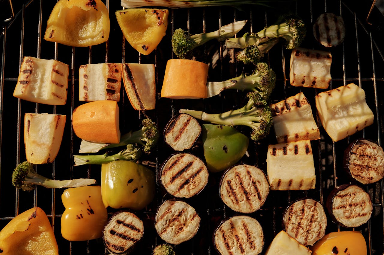 Services-01 Assorted grilled vegetables including peppers, eggplant, and broccoli on a barbecue grill.